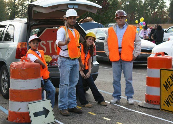 three people in orange vests standing next to traffic cones and signs with cars behind them