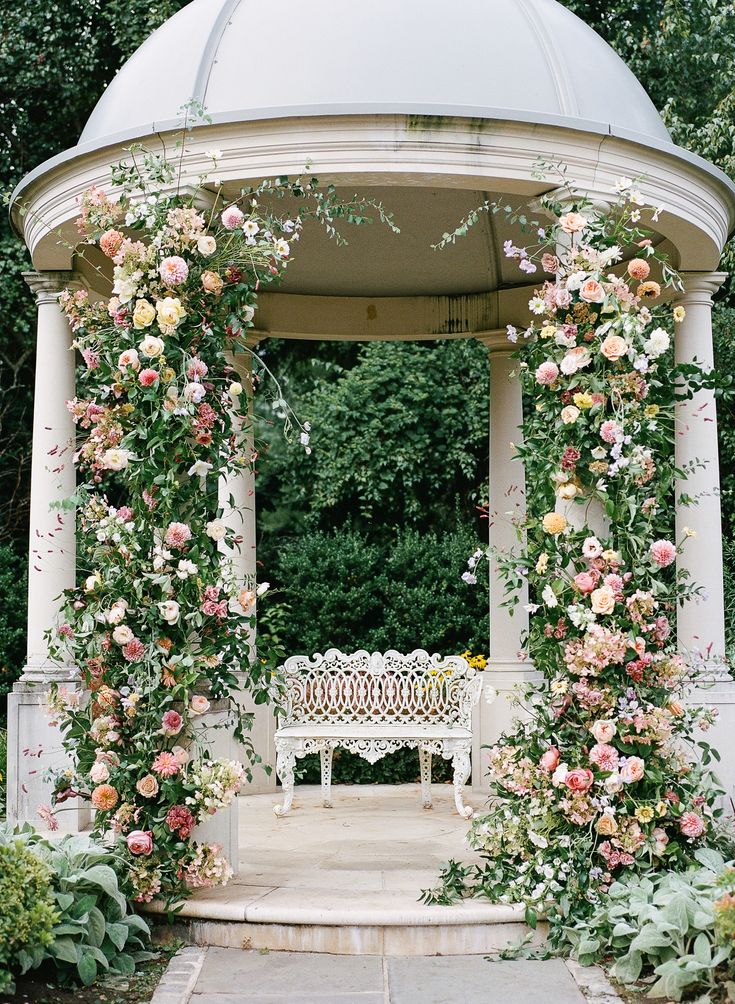 a gazebo covered in flowers and greenery next to a bench