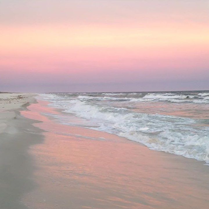 a beach with waves coming in to the shore and pink sky at sunset or dawn