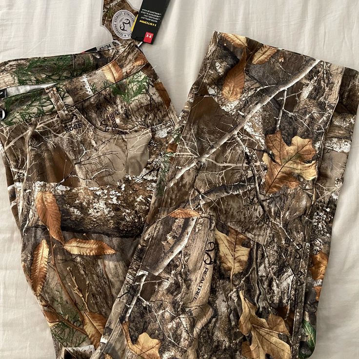 a pair of camouflage pants laying on top of a white sheet covered bed next to an alarm clock