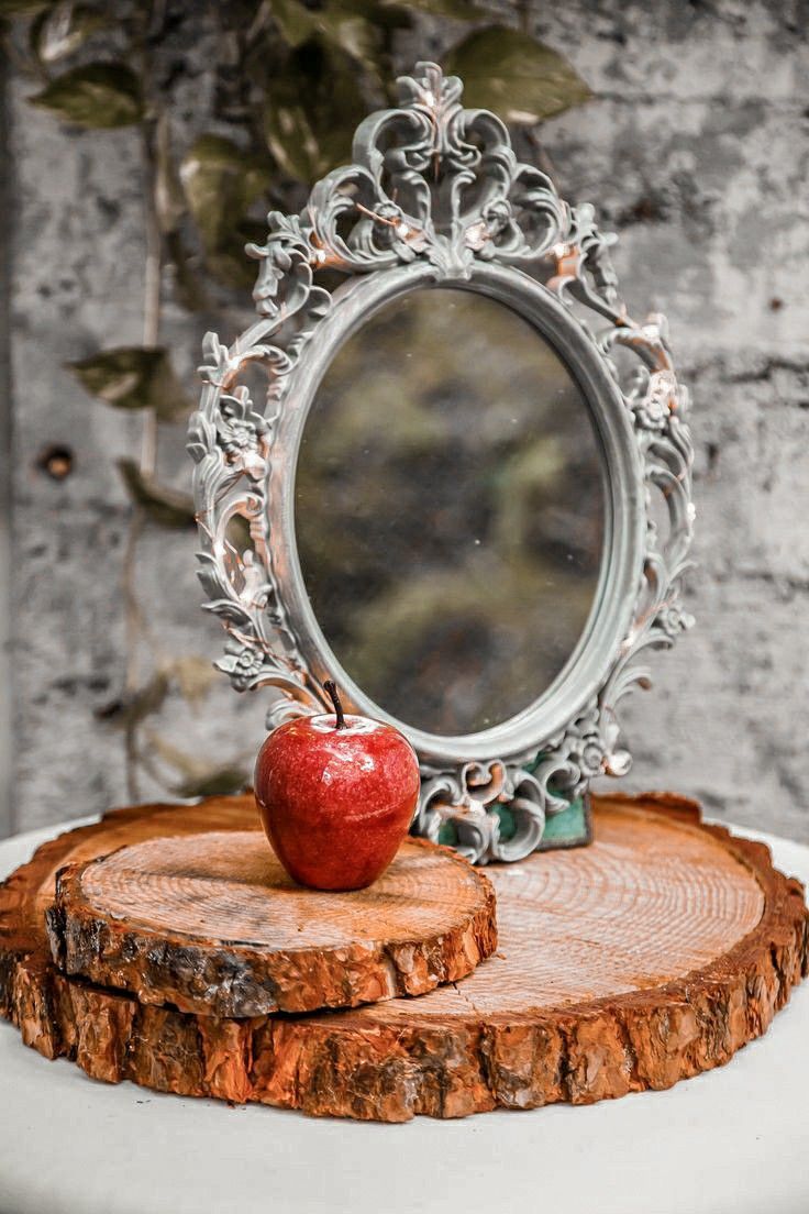 an apple sitting on top of a piece of wood with a mirror in the background