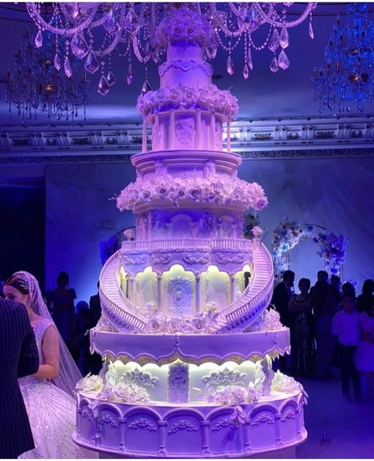 a bride and groom standing in front of a large wedding cake with purple lights on it