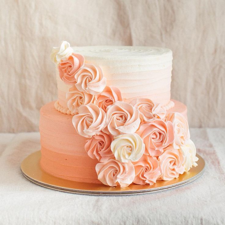 a three layer cake with pink and white frosting flowers on the top, sitting on a gold plate