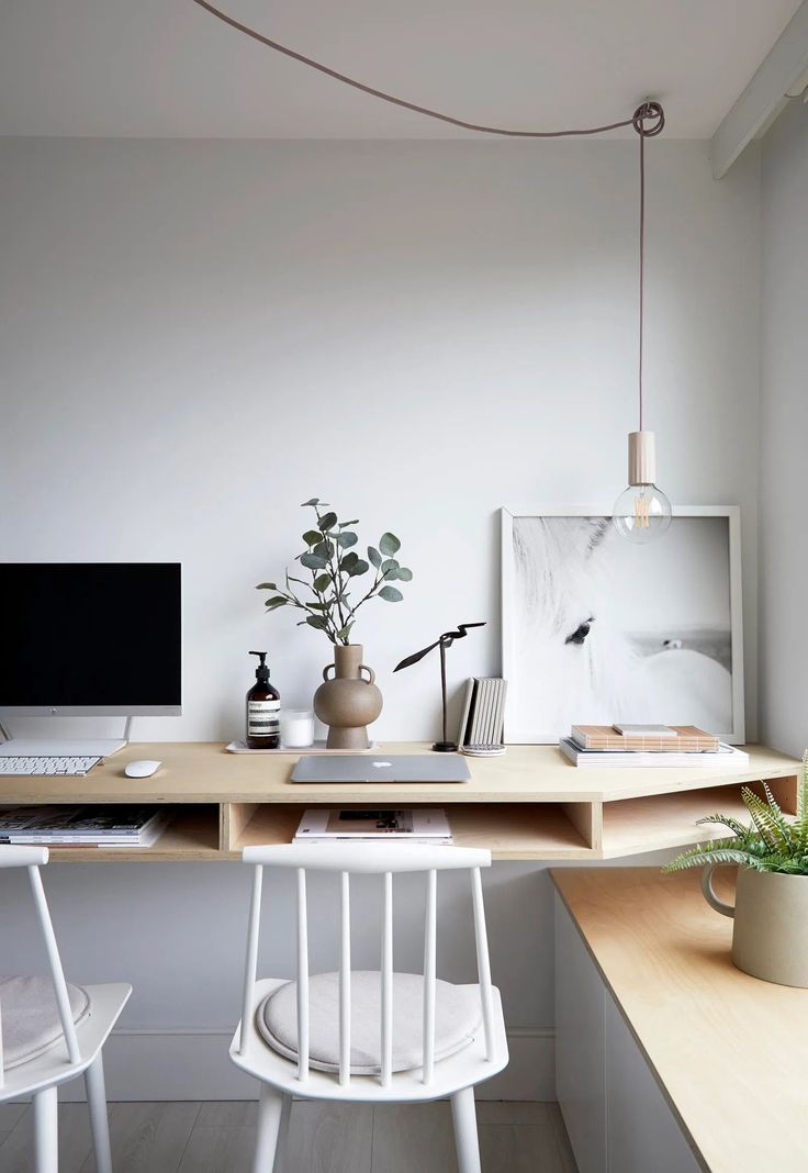 a desk with two white chairs and a computer monitor on top of it, next to a potted plant