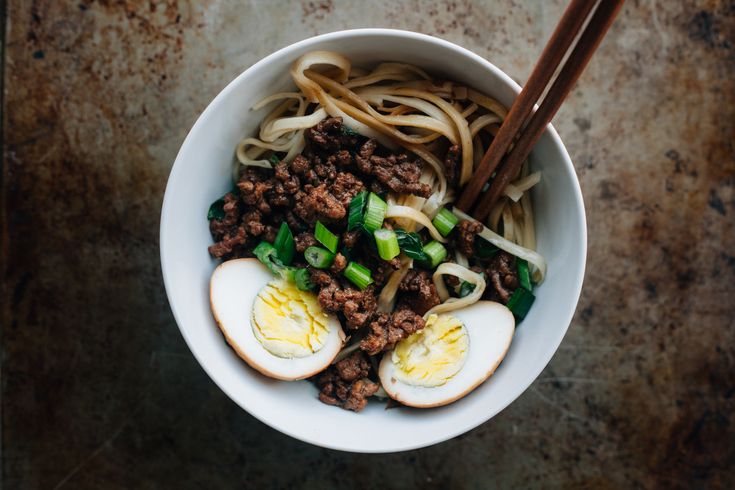 a bowl filled with noodles, meat and vegetables next to chopsticks on a table