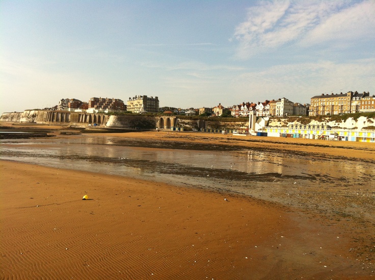 the beach is sandy and brown with little waves coming in to shore as buildings are on the other side