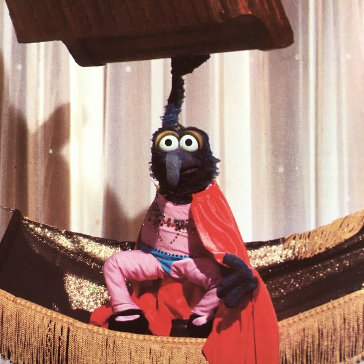 a puppet is sitting in a hammock with a red cape on it's head