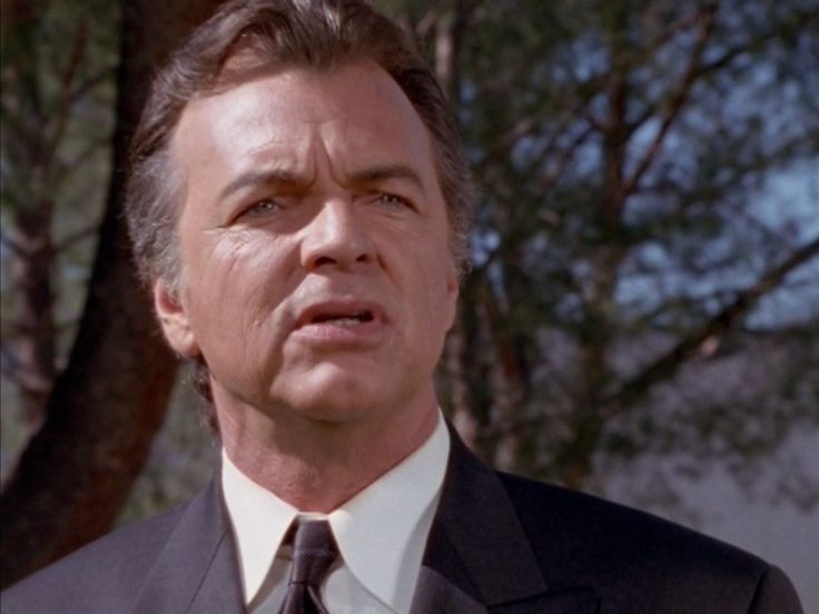 a close up of a person wearing a suit and tie with trees in the background