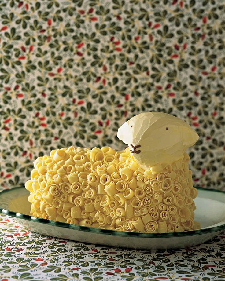 a sheep cake sitting on top of a plate next to a wallpapered wall