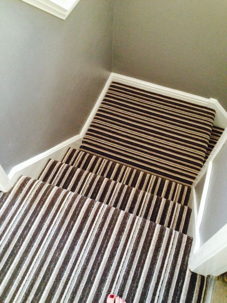 someone's feet are on the striped carpeted stair tread in this small room