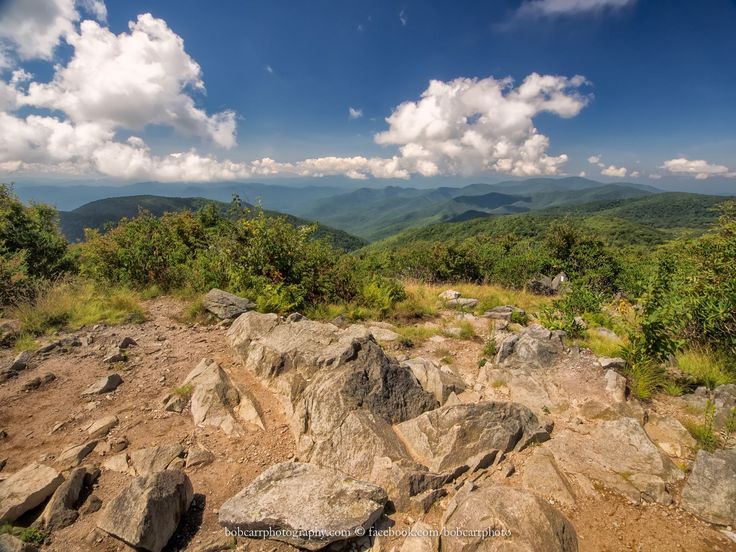 a mountain view with rocks and trees in the foreground on a sunny day that is partly cloudy