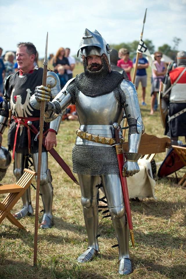 two men dressed in medieval armor standing next to each other on grass with people behind them