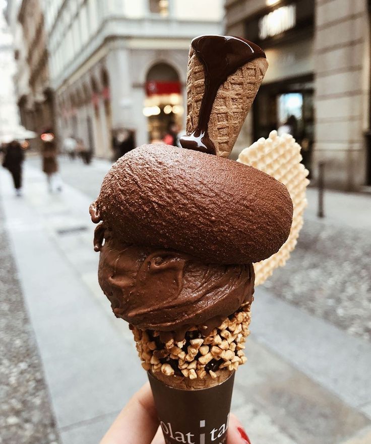 a hand holding an ice cream cone with chocolate and nuts on top