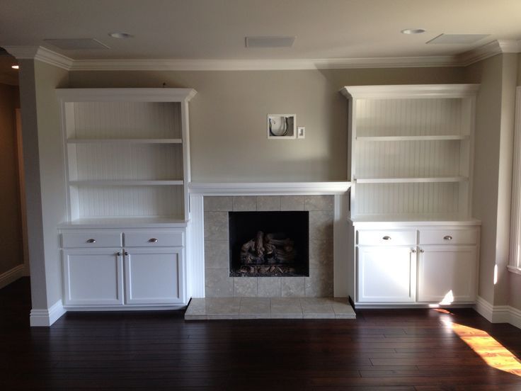 an empty living room with white bookcases and fireplace