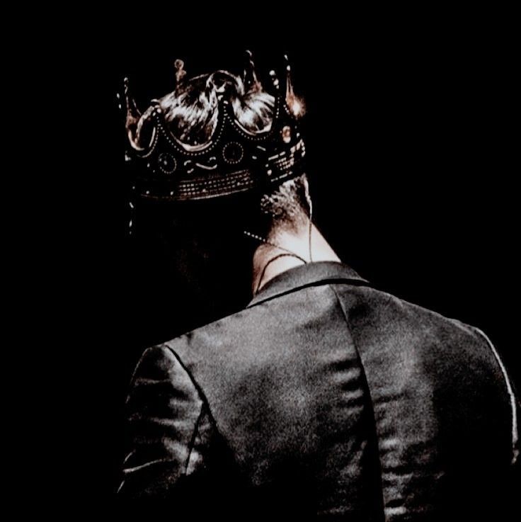 the back of a man with a crown on his head, wearing a black suit