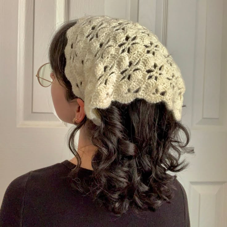 a woman wearing a white crochet hat standing in front of a door with her back to the camera