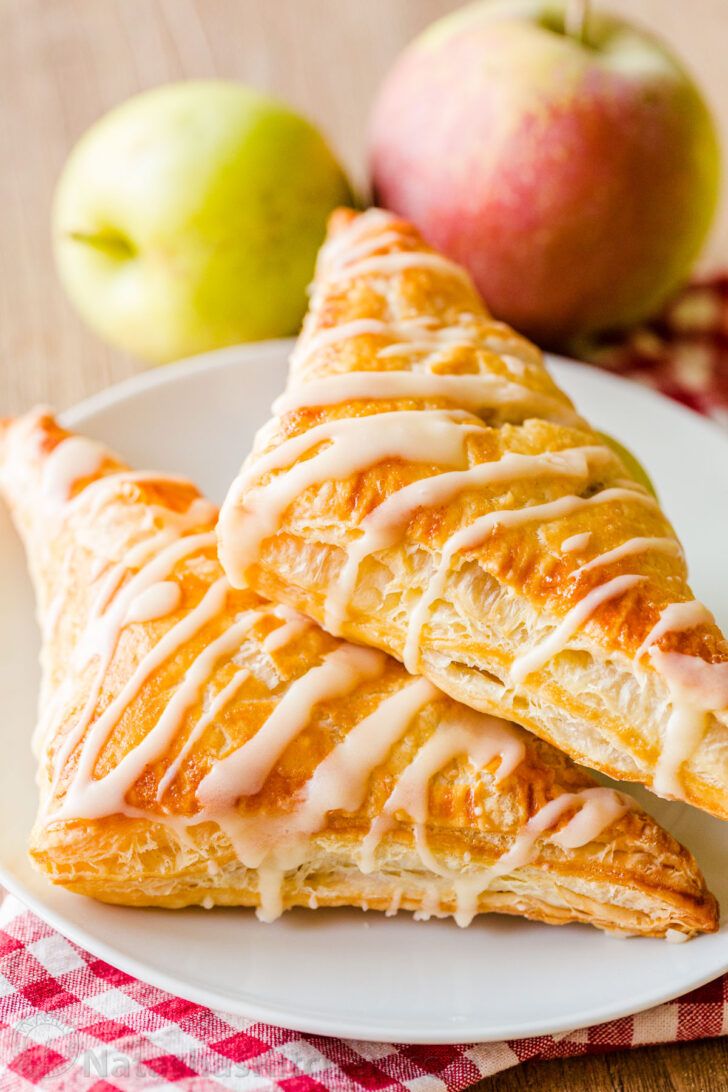 two croissants on a plate with apples in the background