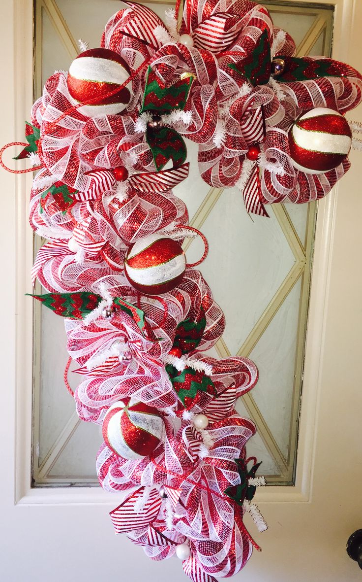 a wreath made out of red and white christmas ornaments hanging on a door with ribbon