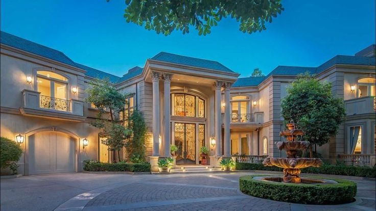 a large house with a fountain in front of it at night time, surrounded by greenery and trees