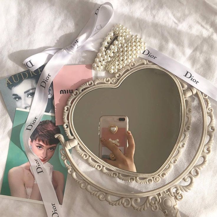 a person taking a selfie in front of a heart shaped mirror with pearls on it