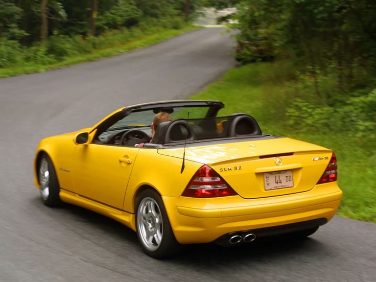 a yellow convertible car driving down a road next to lush green grass and trees in the background