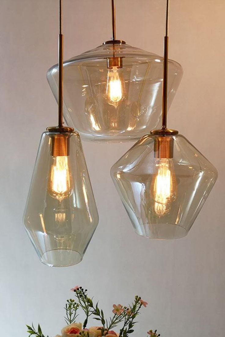 three clear glass pendant lights hanging over a vase with flowers in it on a table