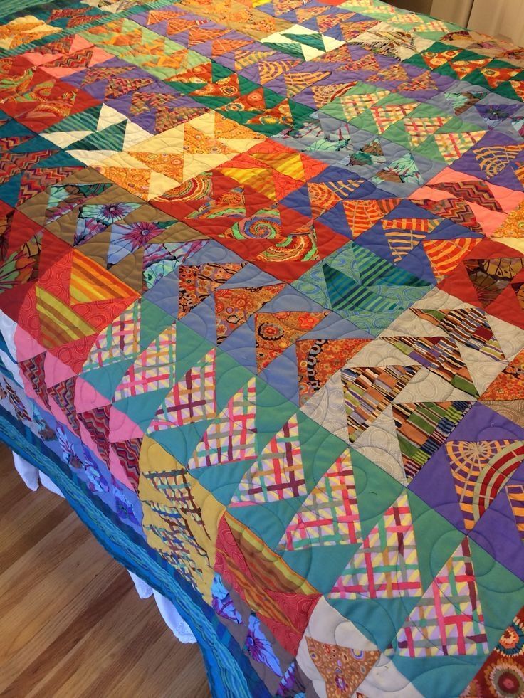 a colorful quilt on top of a bed in a room with wooden floors and walls