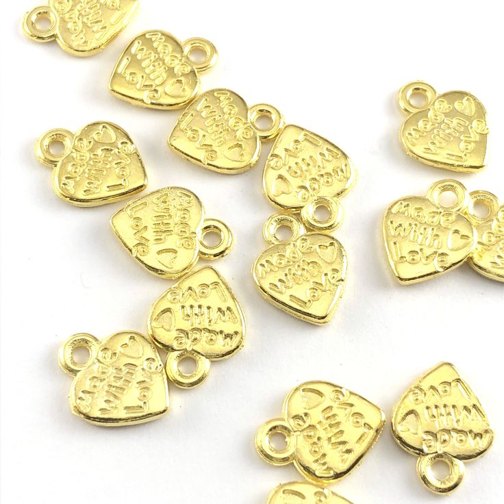 heart shaped gold jewelry charms with the words made with love on them, on a hand to show scale Gold Jewelry With Heart Charm And Round Beads, Gold Heart Charm Necklace Nickel Free, Gold Heart-shaped Nickel-free Charm Necklace, Valentine's Day Heart-shaped Dangling Charms, Gold Heart Charms For Jewelry Making, Handmade Gold Charm Necklaces For Valentine's Day, Heart-shaped Gold Plated Charms For Gifts, Handmade Gold Charm Necklace For Valentine's Day, Gold Round Charms With Dangling Details