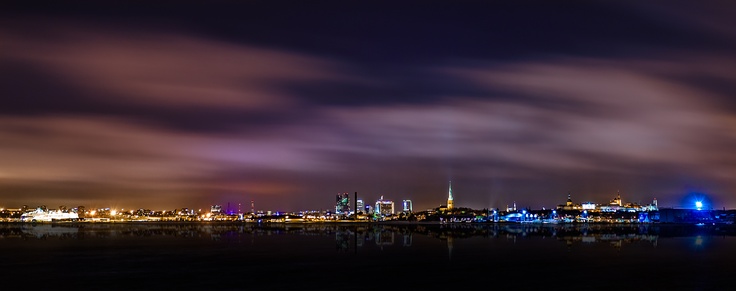 the city skyline is lit up at night with colorful lights and clouds in the sky