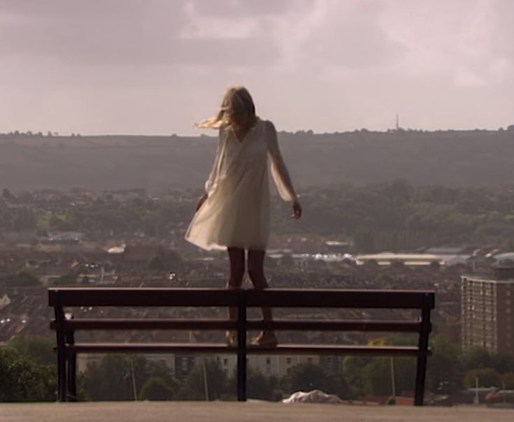 a woman standing on top of a bench looking out over a cityscape in the distance