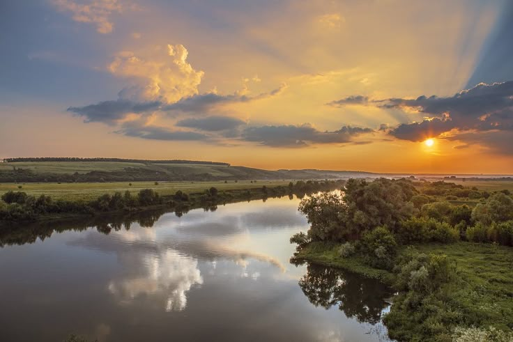 the sun is setting over a river with clouds in the sky