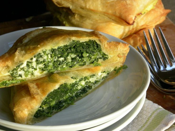 two pieces of spinach pie on a plate with a fork and knife next to it