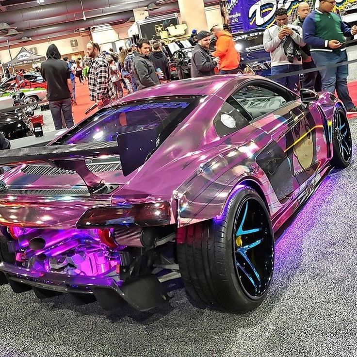 a purple sports car parked on top of a floor next to other cars and people