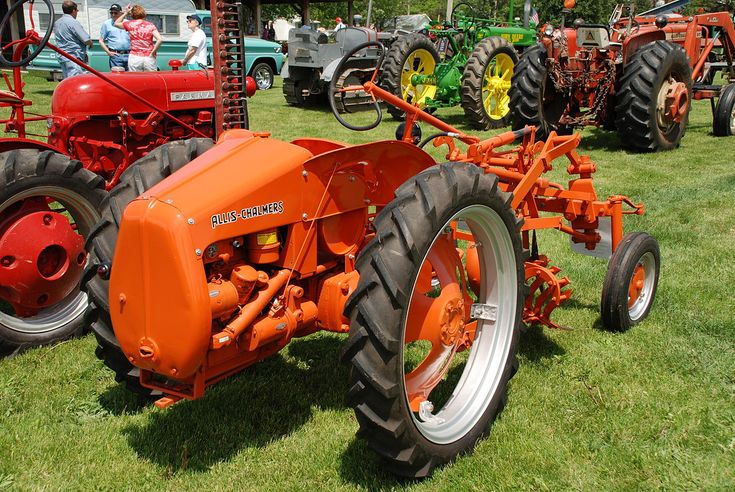 an orange tractor parked in the grass next to other tractors