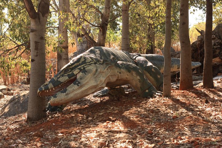 an artificial dinosaur in the woods with trees around it's neck and head sticking out