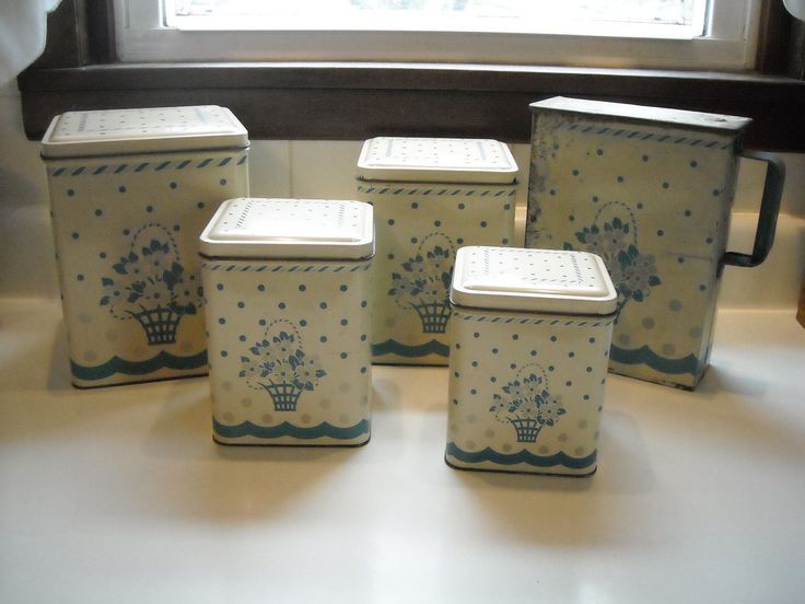 four ceramic containers sitting on top of a white counter next to a window sill