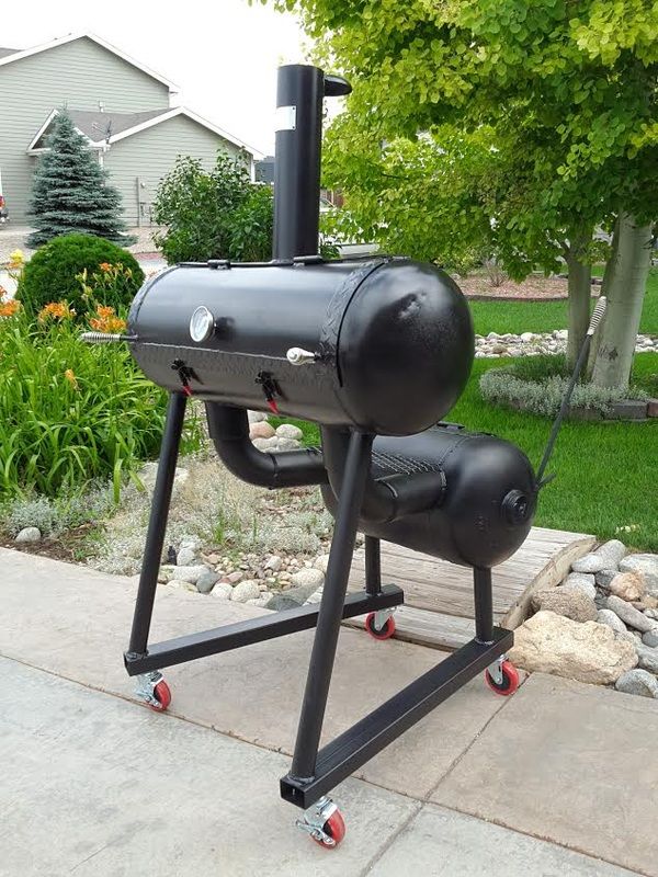 an outdoor bbq grill sitting on top of a sidewalk next to some trees and bushes