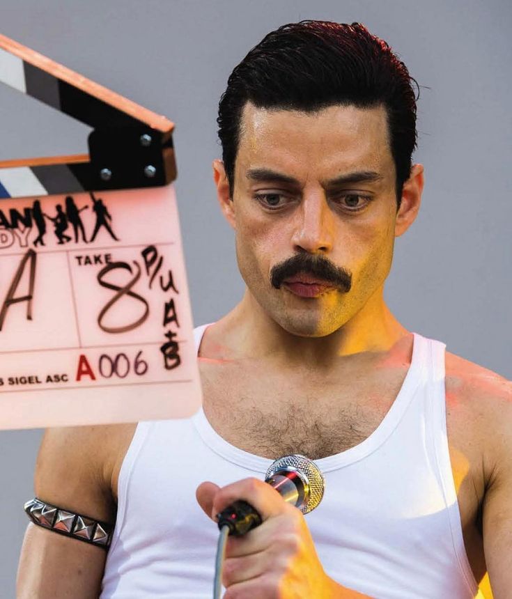 a man in white shirt holding up a movie clapper with yellow paint on his face