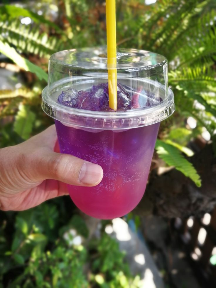 a person holding up a purple drink in a plastic cup with a yellow straw sticking out of it