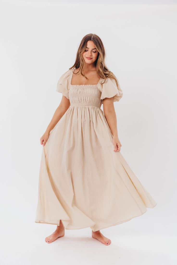 Be the life of the party in the Nan Maxi Dress! This beautiful gown comes in a gorgeous, multi-season neutral hue, and features a smocked bodice and puffed sleeves that can be worn on or off the shoulder - it's like getting two dresses in one! Style the Nan with slides for a casual, feminine outfit, or with neutral heels for the perfect event dress. FIT: Runs true to size. MATERIAL: GARMENT DETAILS: Neutral maxi dress with empire waist silhouette, smocked bodice, and puffed sleeves with elastica Spring Puff Sleeve Dress For Gatherings, Puff Sleeve Maxi Dress With Ruffled Fitted Bodice, Fitted Cream Smocked Dress, Elegant Dress With Smocked Back And Bishop Sleeves, Billowy Ruched Maxi Dress With Puff Sleeves, Flowy Smocked Bodice Puff Sleeve Dresses, Fitted Cream Smocked Dress With Smocked Cuffs, Flowy Ruched Maxi Dress With Puff Sleeves, Puff Sleeve Ruched Maxi Dress For Garden Party