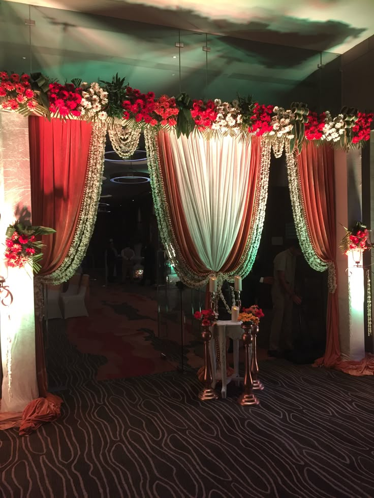 a decorated stage with red and white drapes, flowers and greenery on it