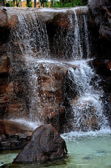 there is a waterfall that has water coming out of the rocks and into the pool