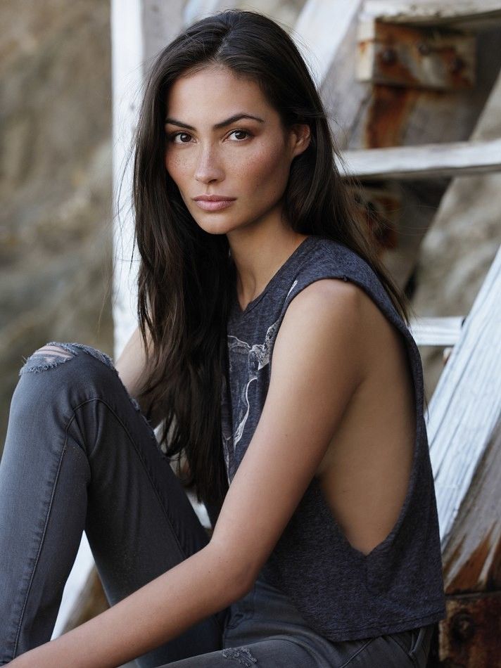 a beautiful young woman sitting on top of a wooden bench next to a wall and stairs