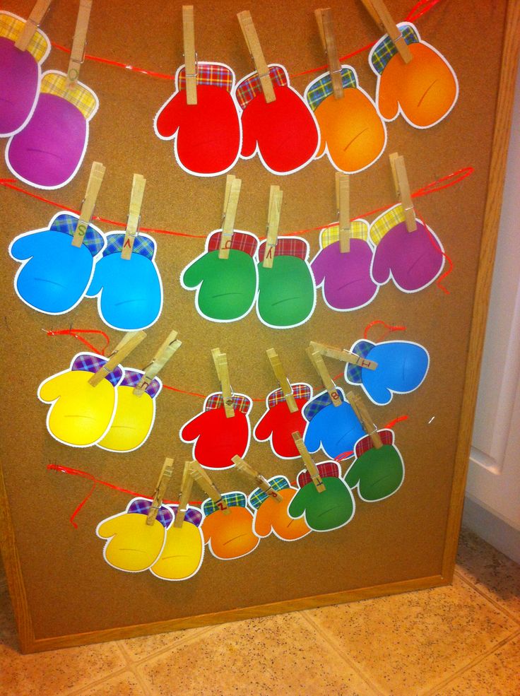 a bulletin board with clothes pins attached to it and colorful mittens hanging from them