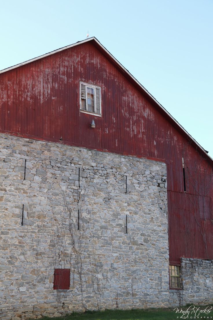 an old brick building with a red door and window on the side of it, next to a grassy field