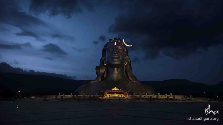 the buddha statue is lit up at night with dark clouds in the sky behind it