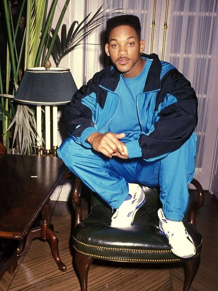 a young man sitting on top of a wooden table next to a lamp and potted plant