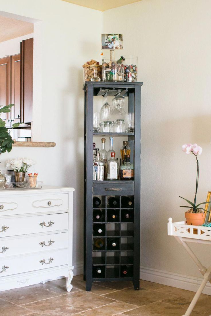 a tall black wine rack in the corner of a room next to a white dresser