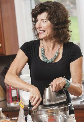 a woman standing in a kitchen with a pot on top of a stove and smiling at the camera