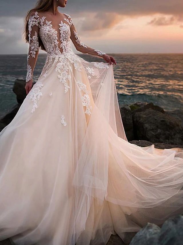 a woman in a wedding dress standing on rocks near the ocean at sunset with her back to the camera